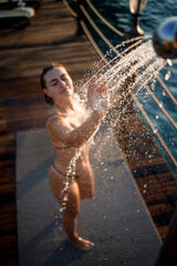 Beautiful young woman takes a relaxing shower in a swimsuit on a sunny day outdoors by the sea. The girl on vacation is resting. Selective focus