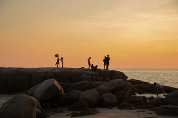 The stones on beach in evening have the background of the sea and the evening sun. There are people standing on rocks and flags