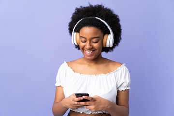 Young African American woman isolated on purple background listening music and looking to mobile