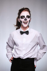 girl in Halloween makeup in the image of a dead man with a white-black skull in a plain shirt with a bow tie