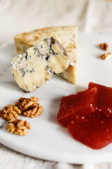 Slice of blue aged Stilton cheese accompanied with quince marmalade or jelly or jam Spanish dulce de Membrillo and walnuts on white marble tray. Selective focus