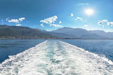Sea and kielwater seen from ship trail on the water. View of Tivat coastline from ship
