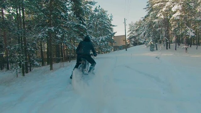 Cyclist in Black Clothes, Helmet and Snow Glasses Riding on Electric Bike in the Snow in Winter Forest. E-Bike Riding and Drifting at Cold Sunny Day - Super Slow Motion