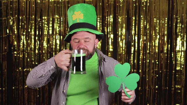 a bearded Caucasian man holds a glass of green beer in his hand and a three-leafed woman dancing on a yellow background. Saint patricks day celebration concept.