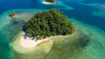 Island with a sandy beach and azure water surrounded by a coral reef and an atoll. Britania Islands, Surigao del Sur, Philippines.