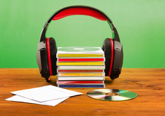 Headphones with CDs on a wooden table, on a green background.