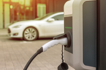 EV Car or Electric car at charging station with the power cable supply plugged in on blurred city background
