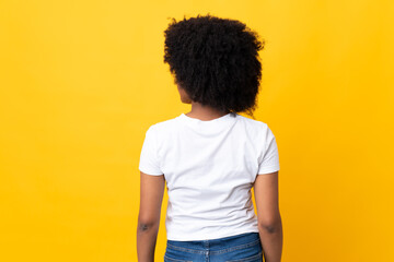 Young African American woman isolated on yellow background in back position and looking side