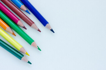 Sharp colorful pencils pointing in one direction on white background