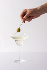 Male hand with olive over cocktail glass with vermouth