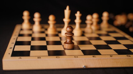 Close up of white and black wooden chess pieces on board. Selective focus on confrontation of black...