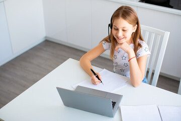 Photo of a smiling pupil doing her homework under the guidance of an online teacher.