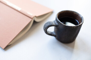 Cup of tea or coffee and opened book for relaxation time on a white table.