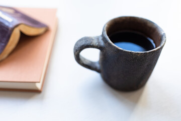 Cup of tea or coffee and opened book for relaxation time on a white table.