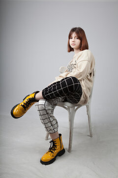 A teenage girl of eleven years old with red hair and freckles, in yellow big shoes sits on a chair in the studio.