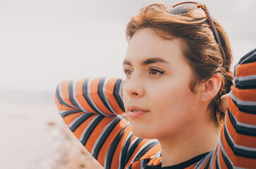 Chica joven y bonita  con gafas de viaje y una blusa naranja mirando al horizonte mientras el sol le hace contraluz, calma y contemplación
