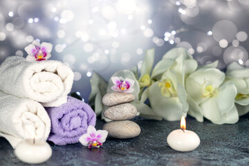 Obraz na płótnie Canvas Spa resort therapy composition with massage stones, rolled towels, burning candles, and orchid flowers, abstract lights. Concept of spa, relax or resort.