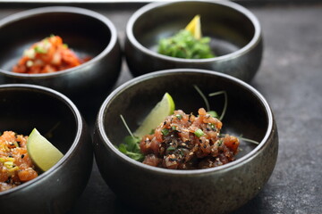 Tuna tartare, salmon tartare on a black stony background. A composition of appetizers.