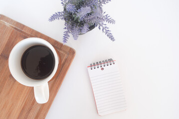 cup of coffee on a wood table , a lavanda plant and a book note in a white background 