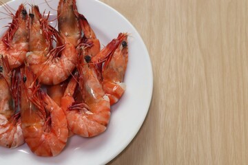 Boiled shrimp in white plate on brown wooden background