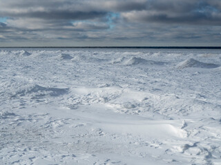 Snowy shore of the frozen sea. Bright sky with expressive clouds.