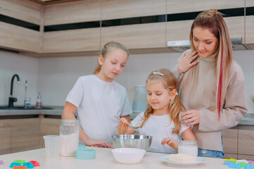 Mom teaches her daughters to cook dough in the kitchen.