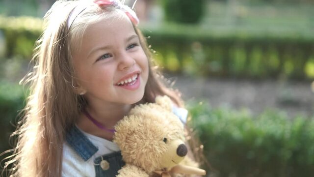 Pretty child girl playing with her favorite teddy bear toy outdoors in summer park.