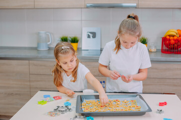 Two sisters are making homemade cookies in the kitchen.