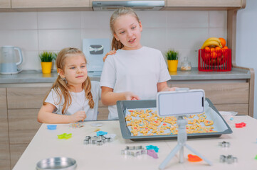 Two sisters bloggers are making cookies and filming training videos on a smartphone.
