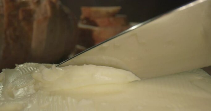 Natural and organic butter. The process of making vegetarian homemade margarine with a knife from a large piece on the kitchen table with bread. Cinematic slow 4K video.