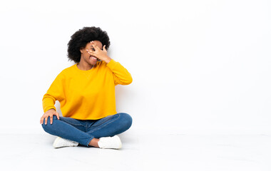 Young African American woman sitting on the floor covering eyes by hands and smiling