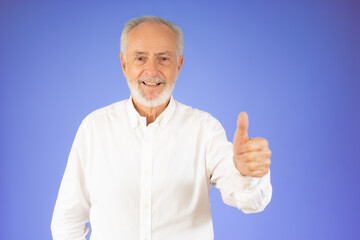 Senior man standing over isolated violet background doing happy thumbs up gesture with hand. Approving expression looking at the camera showing success.