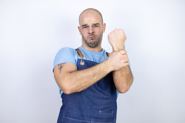 Young bald man wearing apron uniform over isolated white background suffering pain on hands and fingers, arthritis inflammation