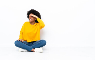 Young African American woman sitting on the floor looking far away with hand to look something