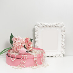 Composition of a box with pearl beads, a bouquet of flowers and a box with female jewelry and an elegant white frame with empty space, mockup in pale pink tones copy space