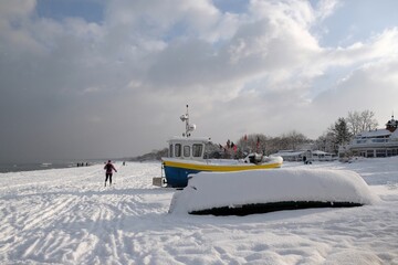 Fishing boats on snowy beach in winter scenery on a sunny and cloudy day. Sopot, Poland