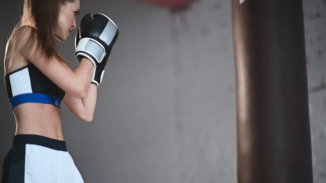 white female athlete boxing the punching bag in urban industrial gym