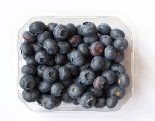 Plastic punnet full of lush blueberries against plain white background