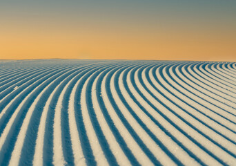 Close up of groomed tracks on a slope in a downhill ski resort with warm evening sky. Shallow depth of field.