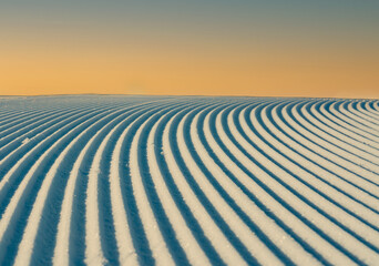 Close up of groomed tracks on a slope in a downhill ski resort with warm evening sky. Shallow depth...