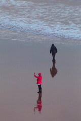 People walk on the sandy beach in town of Sidmouth, Devon. Reflection on the water surface.