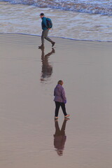 People walk on the sandy beach in town of Sidmouth, Devon. Reflection on the water surface.