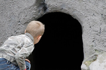 Obraz na płótnie Canvas The child looks into the black hole of the cave. The concept of learning the unknown. Childish curiosity.