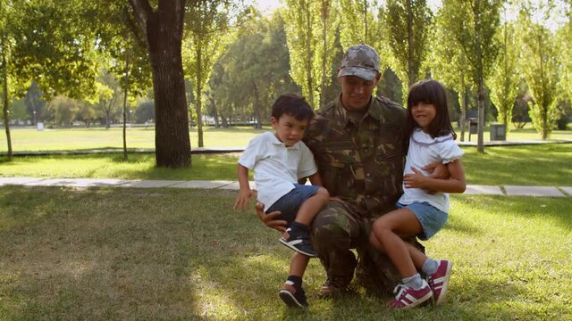 Happy military father wearing uniform, returning home after mission, hugging and playing with kids in summer park. Family reunion concept