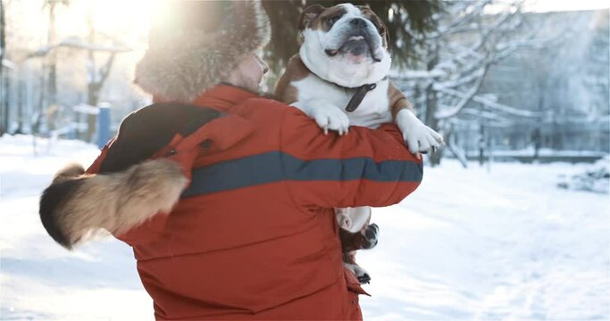 Close up of happy bearded man hugging and gently kissing his cute friend English bulldog. Portrait of guy having fun with his pure breed dog at winter time outside. Animals, pets, human friendship