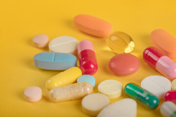 Obraz na płótnie Canvas Assorted pharmaceutical medicine pills, tablets and capsules over yellow background. High number of pills on surface. High resolution image for pharmaceutical industry.