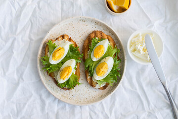 Two egg's sandwiches with cream cheese, green salad and lemon on the white plate,  on light background.