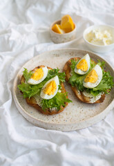 Two egg's sandwiches with cream cheese, green salad and lemon on the white plate,  on light background.