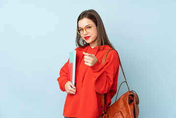 Student girl holding books isolated on blue background points finger at you