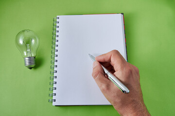 Hand with light bulb with notebook and pen on green background